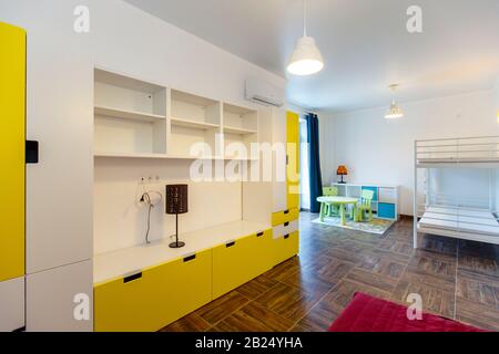 Children's room in the cottage. Bunk bed, window with blue curtains, large wardrobe with yellow doors. Stock Photo