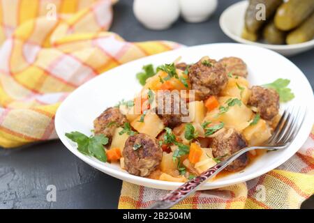 Stewed potatoes with meatballs on a white plate on dark background Stock Photo