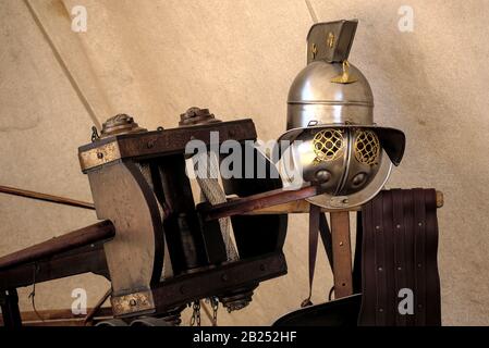 New looking Roman gladiators helmet on top of a wood pole with a traditional wood crossbow next to it Stock Photo
