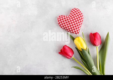 Yellow and red tulips with fabric heart on grey stone background copy space flat lay Stock Photo