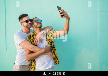 Portrait of happy gay couple spending time together and taking a selfie with mobile phone. Lgbt and love concept. Stock Photo