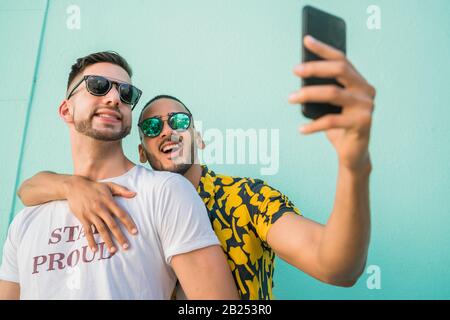 Portrait of happy gay couple spending time together and taking a selfie with mobile phone. Lgbt and love concept. Stock Photo