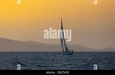 Sail boat in open sea at golden hour in evening. Mountains Silhouette in background. Summer adventure, active vacation in Mediterranean sea Stock Photo