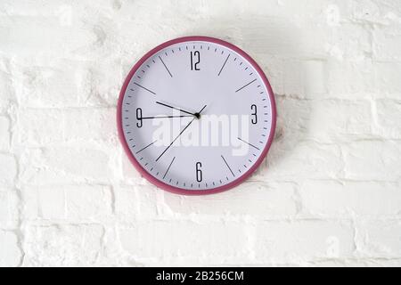 Round clock with arrows and numbers on a white brick wall. Clock on the wall Stock Photo