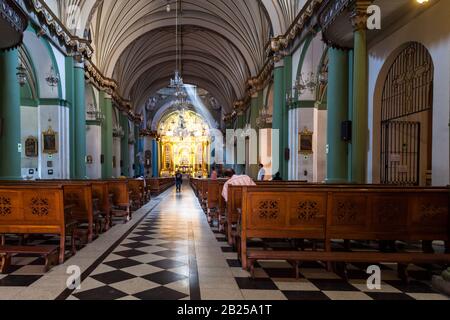 LIMA / PERU - May 10 2016: The interior of a beautifully decorated Catholic Church with a sunbeam and people worshiping in Lima, Peru. Stock Photo