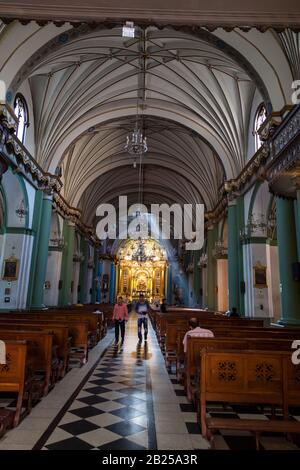LIMA / PERU - May 10 2016: The interior of a beautifully decorated Catholic Church with a sunbeam and people worshiping in Lima, Peru. Stock Photo