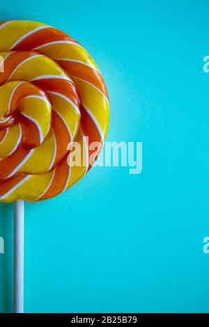 Bright blue vertical background with half swirl lollipop with copy space. Festive backdrop with colorful twisted candy. Rainbow round sweet on stick. Banner, poster, greeting card, web site template Stock Photo