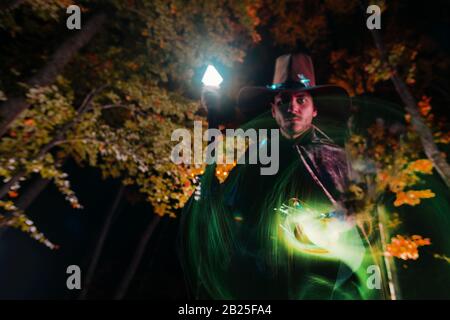 Wizard (mage) casting a spell with his magical staff while standing in an enchanted forest. Stock Photo