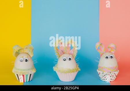 Easter eggs decorate as bunny dressing put on colorful cupcake paper cup and background. Cute creative photo concept. Stock Photo