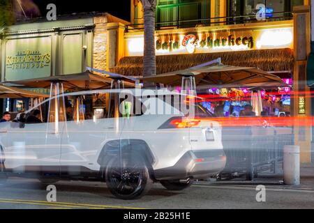 People having a fantastic time at restaurants and bars on a Saturday night on Main Street in Huntington Beach, with light trails and a ghosted car. Stock Photo