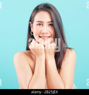 Smiling face Asian beautiful woman her glad keeps both hands under chin smiles pleasantly on blue background Stock Photo