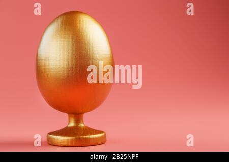 Golden egg on a pink background with a minimalistic concept. Space for text. Easter egg design templates. Stylish decor with minimal concept. Copy spa Stock Photo
