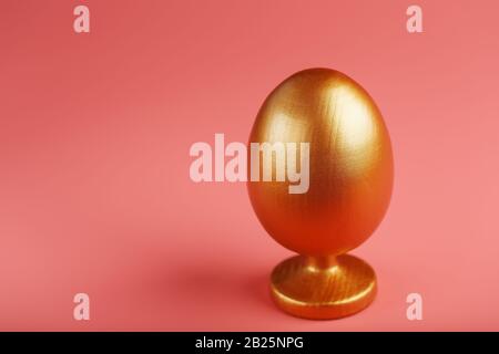 Golden egg on a pink background with a minimalistic concept. Space for text. The concept of the Easter holiday. Stock Photo