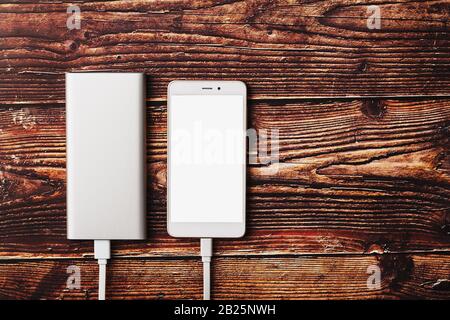 Power Bank charges a smartphone on a wooden background. Universal external battery for gadgets Free space and minimalistic composition. Stock Photo