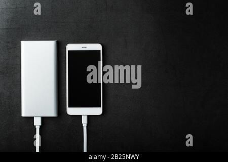 Power Bank charges your smartphone on a dark background. Universal external battery for gadgets free space and minimalistic composition. Portable char Stock Photo