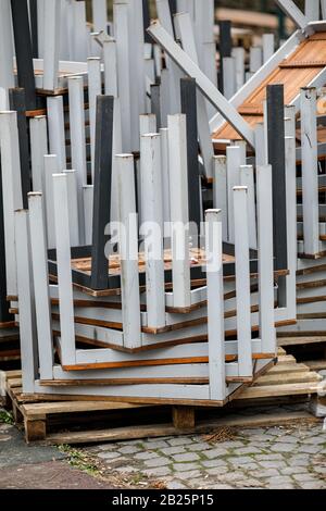 Pile of old restaurant iron and wooden tables stacked outside the restaurant on a cloudy winter day. Stock Photo