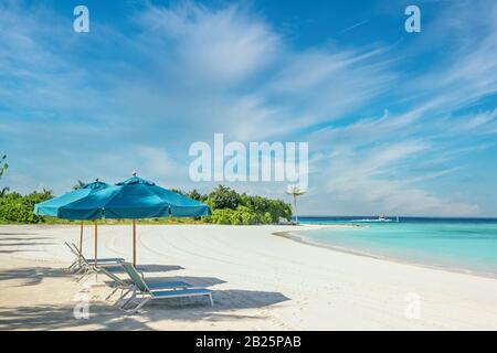 Blue sun umbrellas and resting beach chairs on sandy beach of Maldives Stock Photo