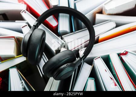 Wireless overhead black headphones lie on the books. The concept of learning through an audiobook. To listen to the book. The view from the top Stock Photo