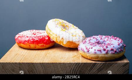 donuts with multi-colored red white and purple icing on a wooden stand on a gray background. Stock Photo