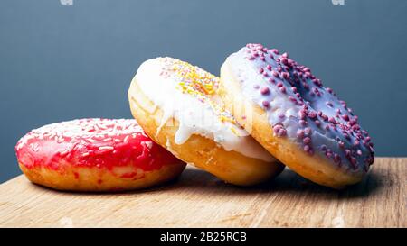 donuts with multi-colored red white and purple icing on a wooden stand on a gray background. Stock Photo