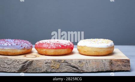 multicolored assorted red,white,violet donuts coated with glaze and sprinkled with Easter powder on a wooden stand on a gray background, sweet eco foo Stock Photo