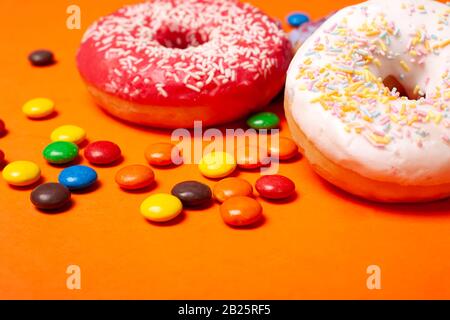 glazed red and white round bun donuts and multi-colored sweets on orange background. children's snacks. Stock Photo