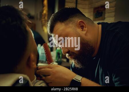 Barber doing the beardstyle and to his client. Hipster client getting haircut. Haircut, styling concept. Stock Photo