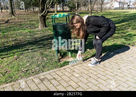 a girl picks up on the ground a plastic bottle and throws it in a waste basket Stock Photo