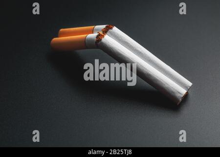 double cigarette smoker Two cigarettes in the form of a double-barreled shotgun on a black  background with copy space. Stop smoking. The concept of smoking kills.  Smoking as Stock Photo