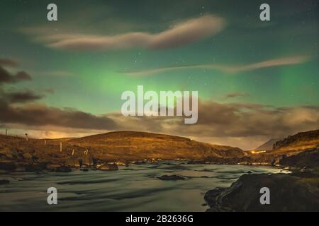 Aurora in Iceland northern lights bright beams rising in green beams reflecting in natural river during full moon Stock Photo