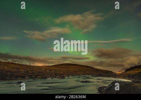 Aurora in Iceland northern lights bright beams rising in green beams reflecting in natural river Stock Photo