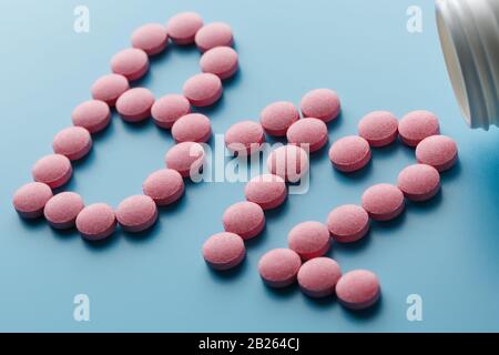Pink pills in the shape of the letter B12 on a blue background, spilled out of a white can. Concept of dietary supplements Stock Photo