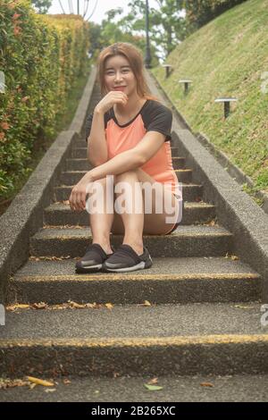 Asian Chinese model in her sports outfit sitting in staircase early in the morning after her daily routine workout session Stock Photo