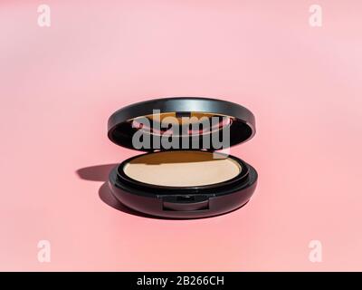 Compact powder on pink background. Female pressed powder in ajar opened black plastic case with mirror, copy space for text or design. Hard light Stock Photo