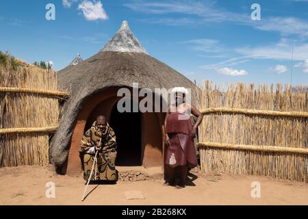 Basotho man and woman in front of traditional hut, Thaba Bosiu Cultural Village, Lesotho Stock Photo