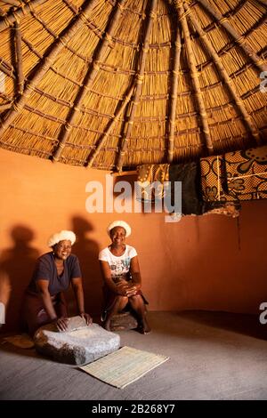 Basotho woman grinding maize in a traditional hut, Thaba Bosiu Cultural Village, Lesotho Stock Photo