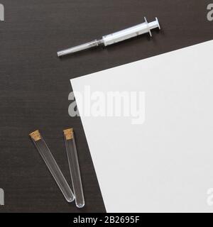 Template of white paper with syringe for injection and bottle on dark wenge color wooden background. The provision of medical and pharmacological services. Stock photo with empty space for text. Stock Photo
