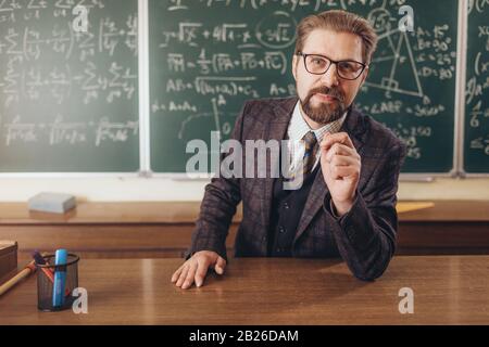 Smiling handsome bearded teacher in suit and glasses explaining new math material Stock Photo