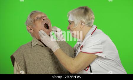 Kind mature woman nurse caregiver supporting to old elder man help with problem, female doctor therapist in uniform examines man and give treatment tips to senior patient Stock Photo