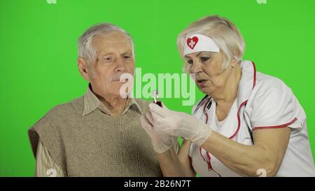 Kind mature woman nurse caregiver supporting to old elder man help with problem, female doctor therapist in uniform examines man and give treatment tips to senior patient Stock Photo