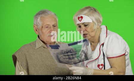 Kind mature woman nurse caregiver supporting to old elder man help with problem, female doctor therapist in uniform examines man and give treatment tips to senior patient Stock Photo