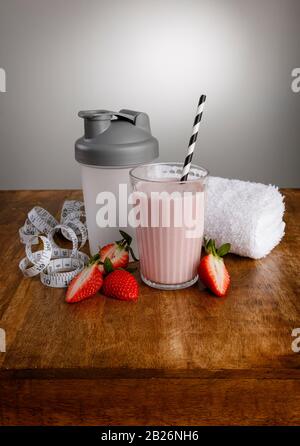 Strawberry orange milkshake, ingredients, tape measure, towel  and shaker with paper straw on a wooden work top Stock Photo