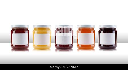 A group jars containing jams and preserves, including rasperry, strawberry, marmalade, chutney and relish, with blank white labels on a white table li Stock Photo