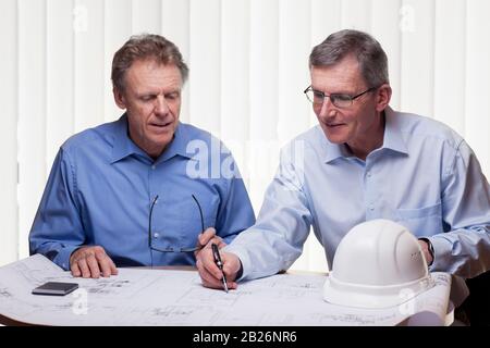 Two mature architects or engineers discussing a construction plan in a bright office Stock Photo