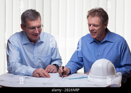 Two mature architects or engineers calcutating a project at a desk with blueprint Stock Photo