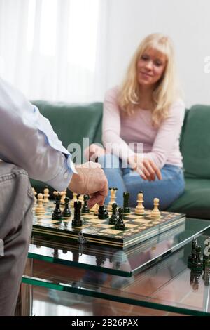 Young blond smiling woman playing chess with a man in a bright living room