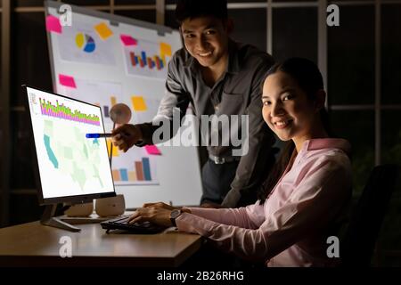 Young adult asian businessman and businesswoman work with analysis graph on white board late at night in their office with desktop computer. Using as Stock Photo