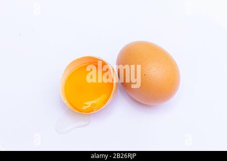 Two brown eggs With one egg broken in half, with a yolk inside the eggshell, laid on a white background Stock Photo