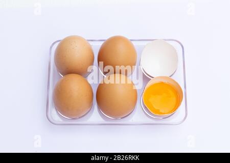 Four brown eggs lay on an egg tray with an eggshell on a white background. Stock Photo
