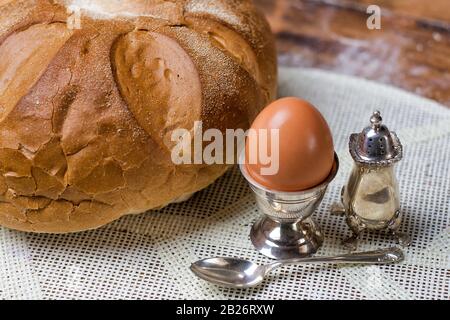 Bread on the wooden table with flour, egg in silver vintage utensil, salt shaker and spoon Stock Photo